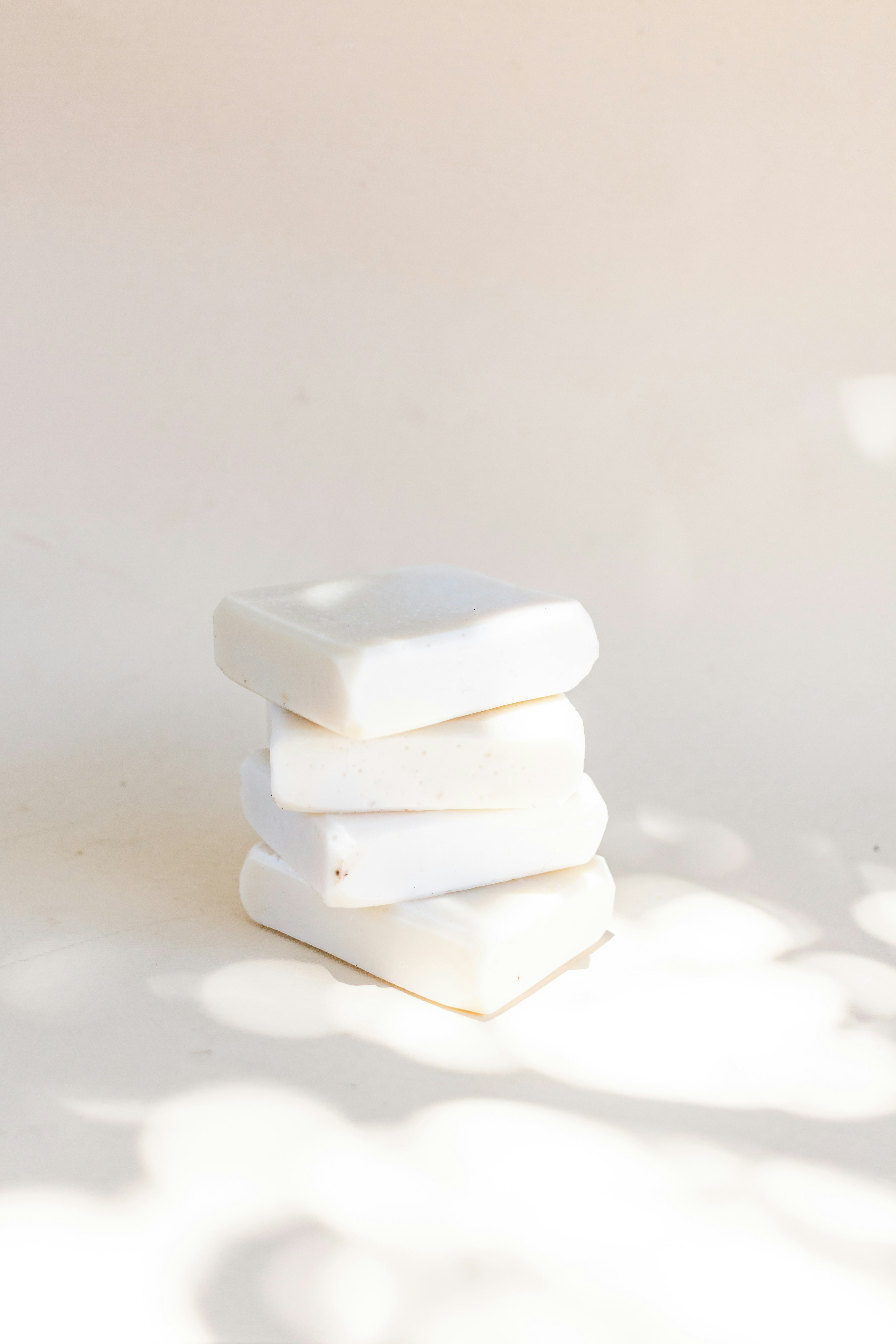A stack of creamy white natural soap bars in soft sunlight